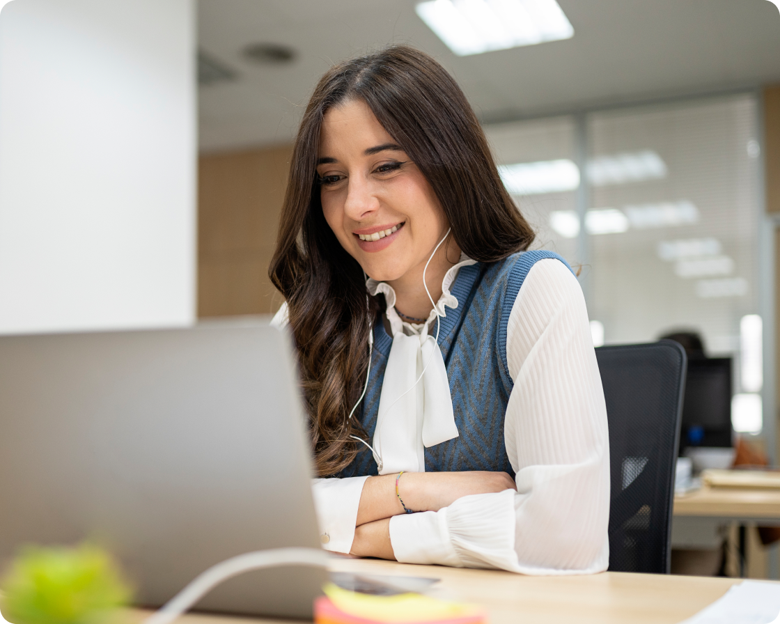 Image of woman at her desk, smiling, and looking at a laptop
