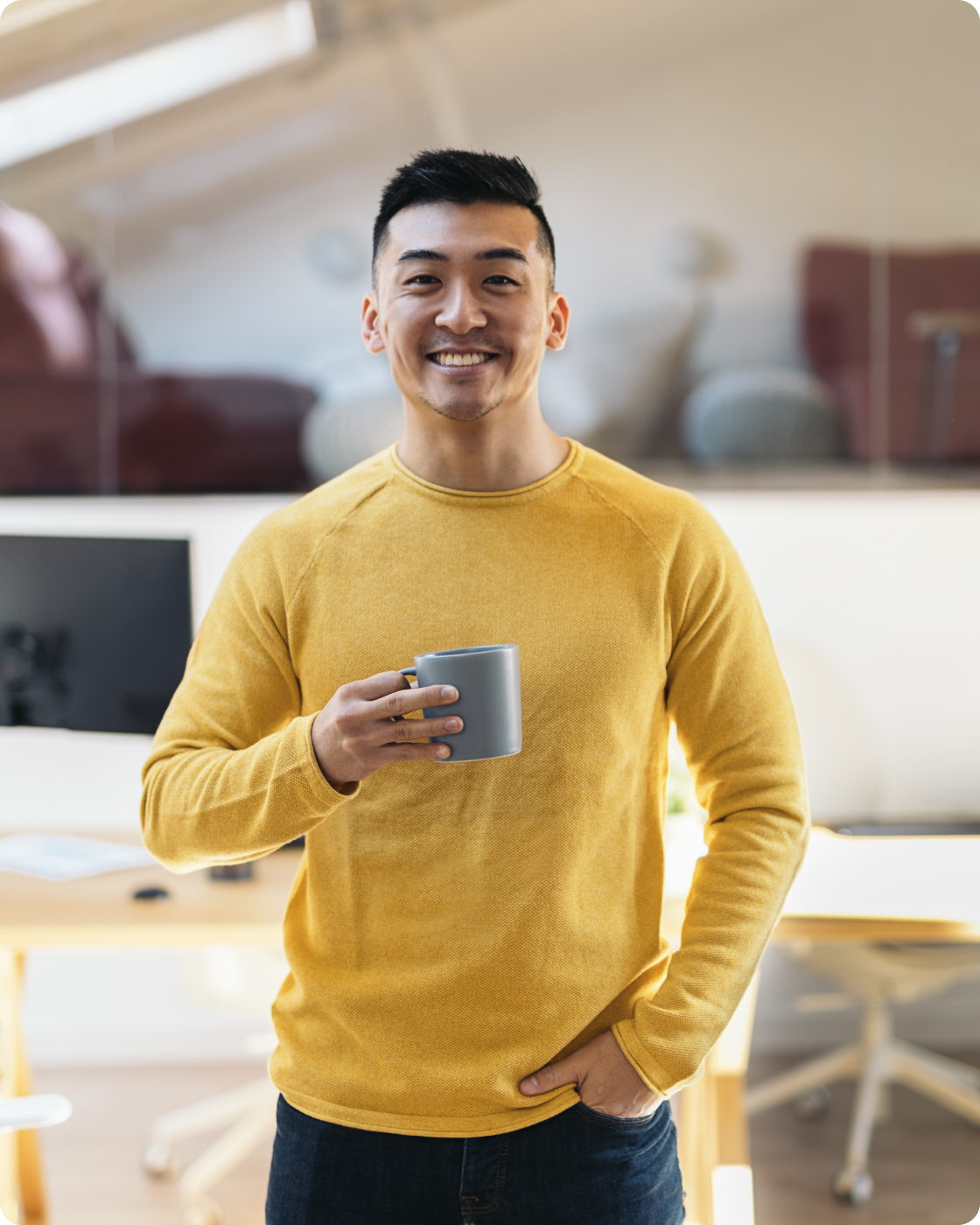 Image of a man smiling to camera in a yellow shirt while holding a mug