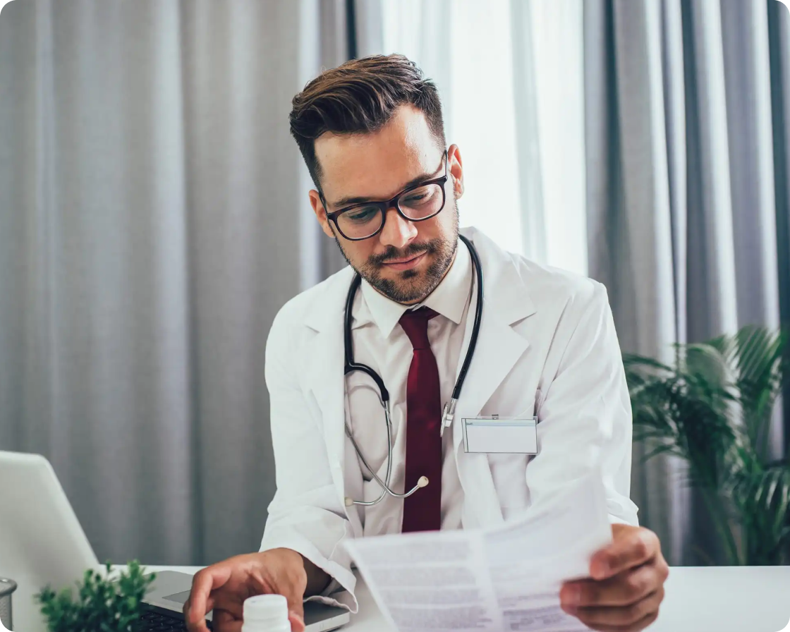 Image of a doctor at a desk looking at a piece of paper