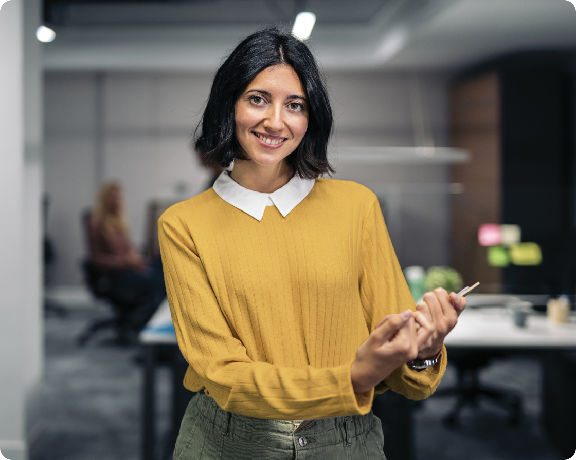 Image of a woman smiling to camera in an office setting holding a tablet
