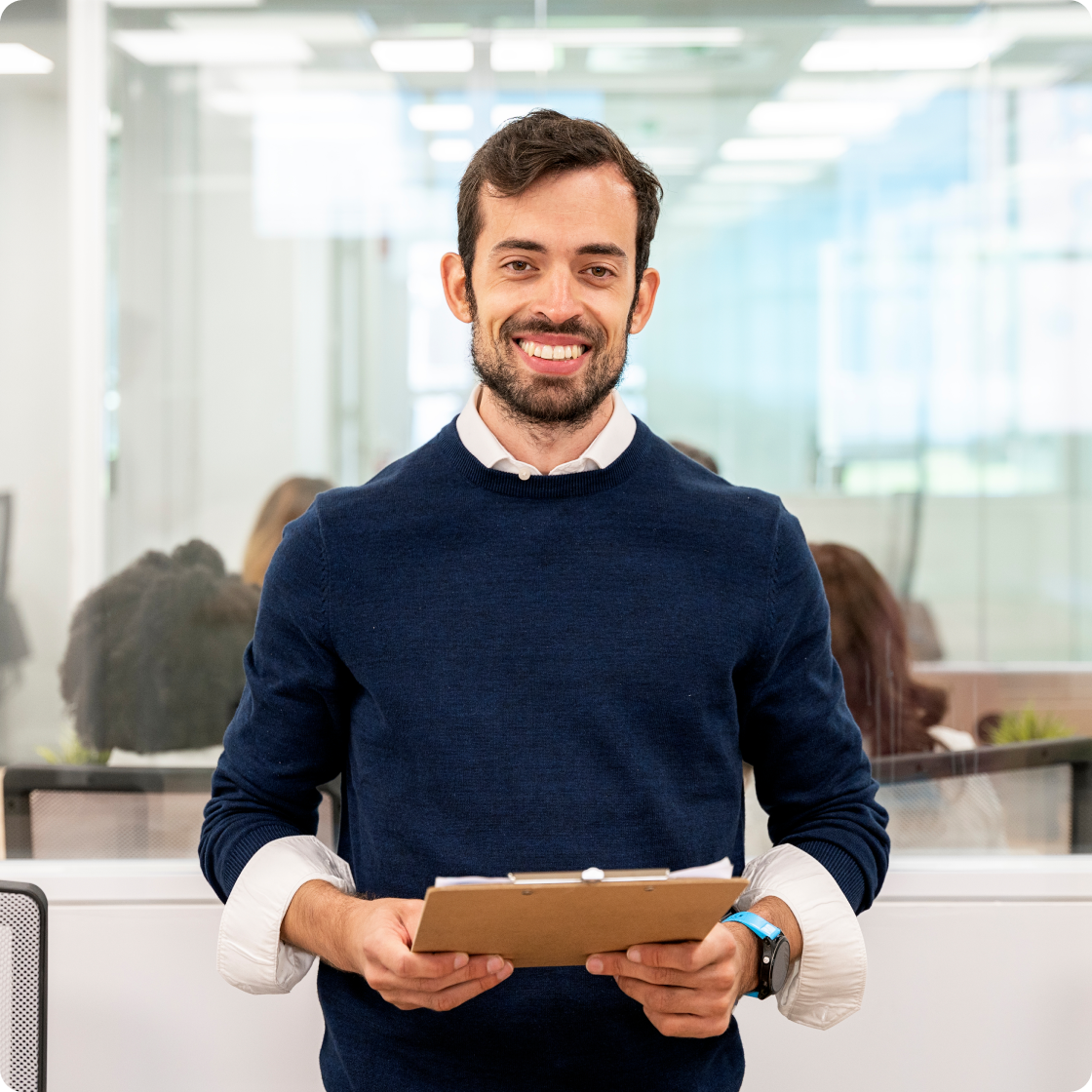 Image of man smiling to camera holding a folder in an office setting