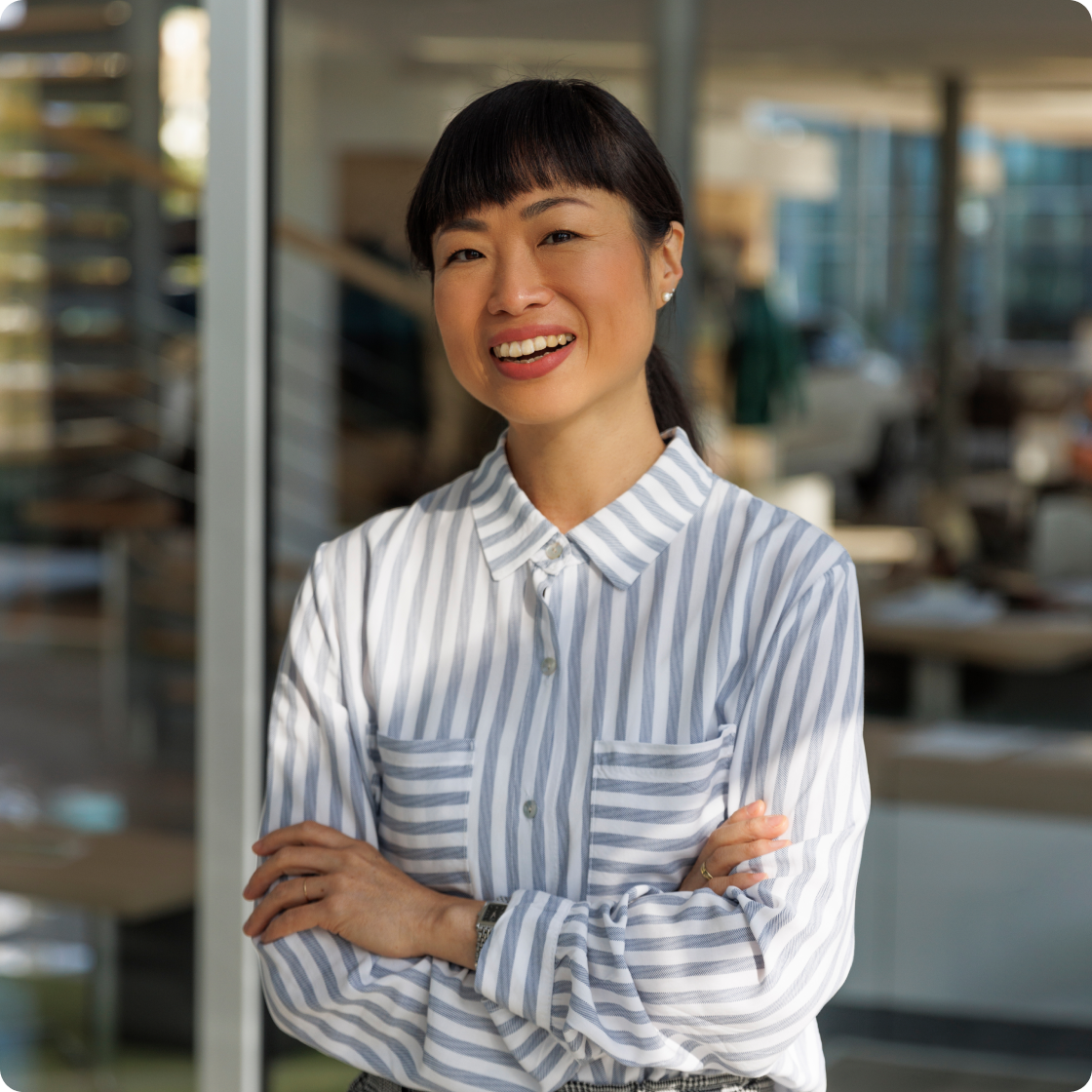 Image of a woman wearing a white and blue striped shirt with her arms crossed, smiling in an office setting